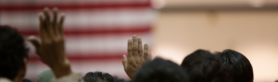 Picture of people raising their hands in front of an American flag.